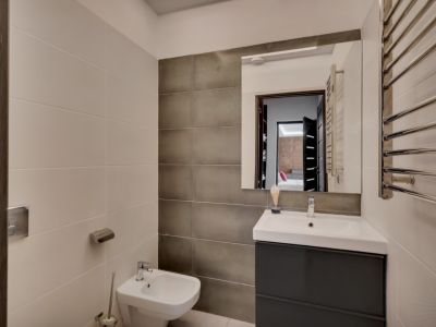 Salle de bain contemporaine avec meuble-lavabo gris foncé, vasque blanche, bidet et sèche-serviettes chromé. Les murs associent des carreaux clairs texturés et des carreaux foncés lisses.