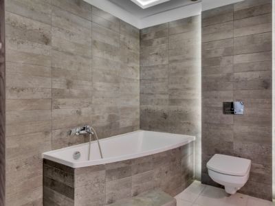 Salle de bain moderne avec baignoire intégrée et WC suspendu, revêtue de carreaux céramiques gris texturés et éclairage LED vertical intégré.