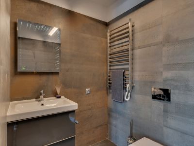 Toilette d'invités avec lavabo suspendu sur meuble gris foncé, miroir lumineux et sèche-serviettes chromé. Les carreaux muraux texturés gris et rouille apportent une touche contemporaine.