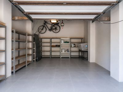 Vaste garage avec carrelage gris durable, étagères métalliques pour rangement organisé et support mural pour vélo. La structure apparente du plafond ajoute une touche pratique.