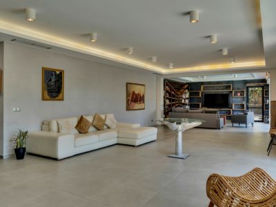 Vaste salon avec canapé d'angle blanc et table design, s'ouvrant sur un espace média et bibliothèque avec mur d'accent sombre et étagères en bois.