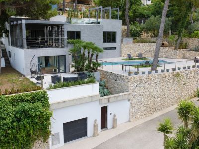 Vue aérienne de la villa moderne, intégrant une piscine privée, des terrasses aménagées et des murs en pierre naturelle, avec un garage au niveau de la rue.