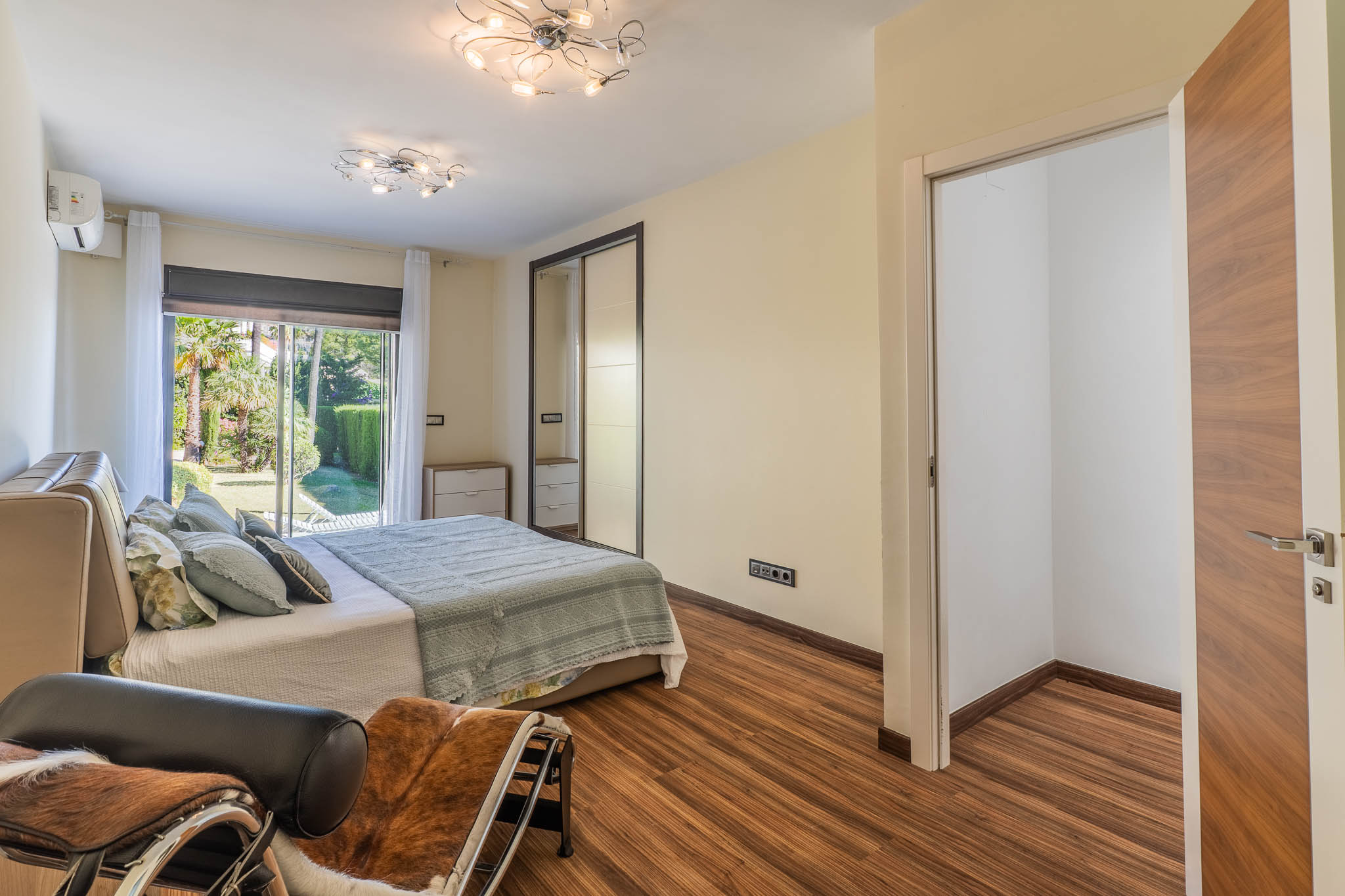 Chambre avec accès direct au jardin par des portes coulissantes vitrées, parquet stratifié et armoire miroir intégrée. Un espace dressing ouvert est visible.