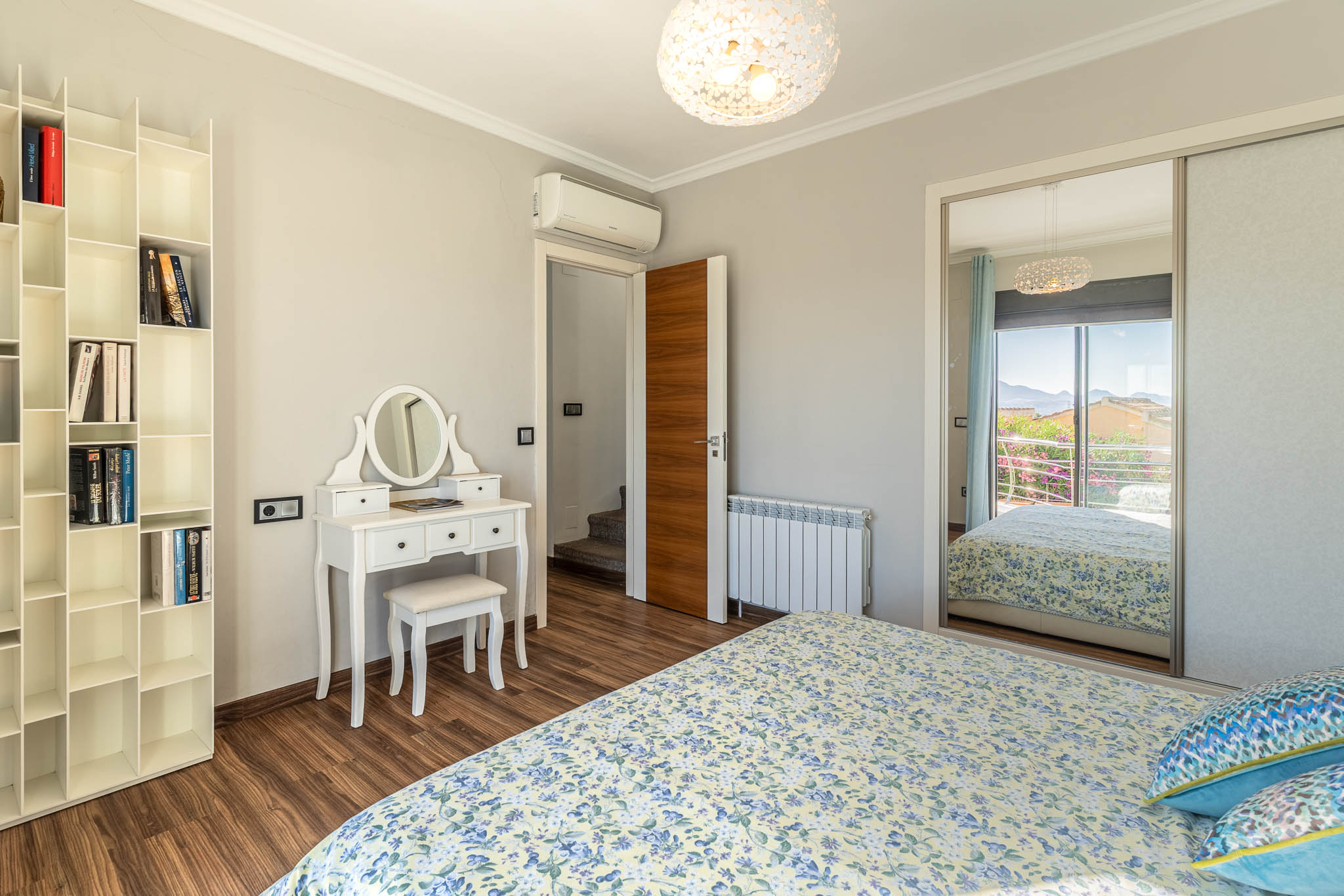 Chambre avec parquet stratifié, coiffeuse blanche et bibliothèque modulaire. L'armoire miroir reflète une vue montagneuse depuis le balcon.