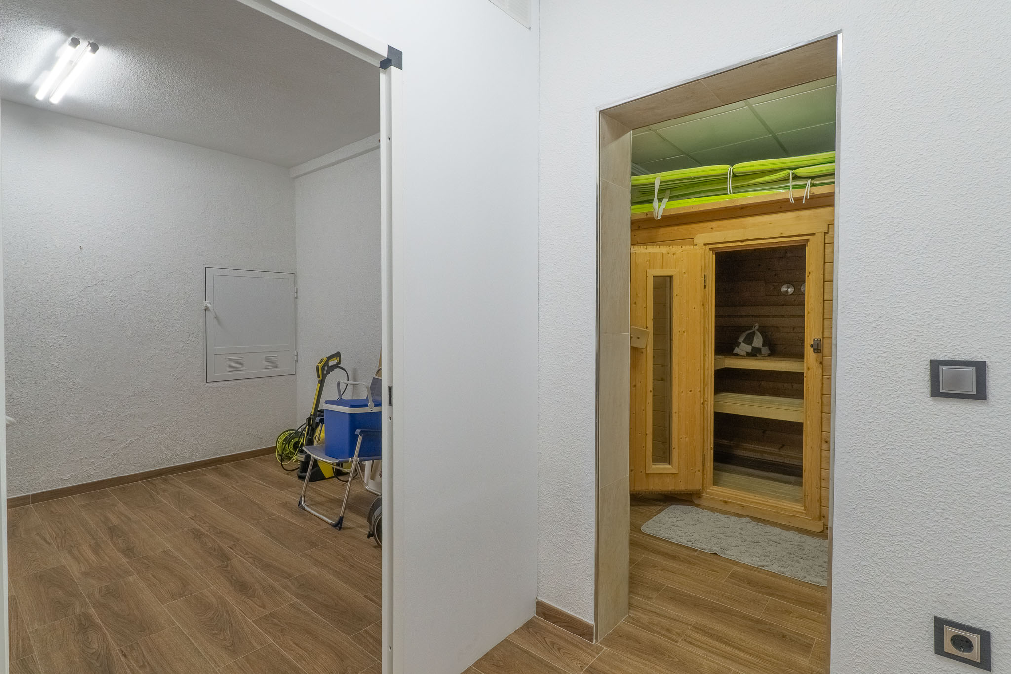 Espace bien-être dédié avec cabine de sauna en bois et bancs intérieurs, adjacent à une buanderie fonctionnelle. Les deux zones partagent un carrelage effet bois.