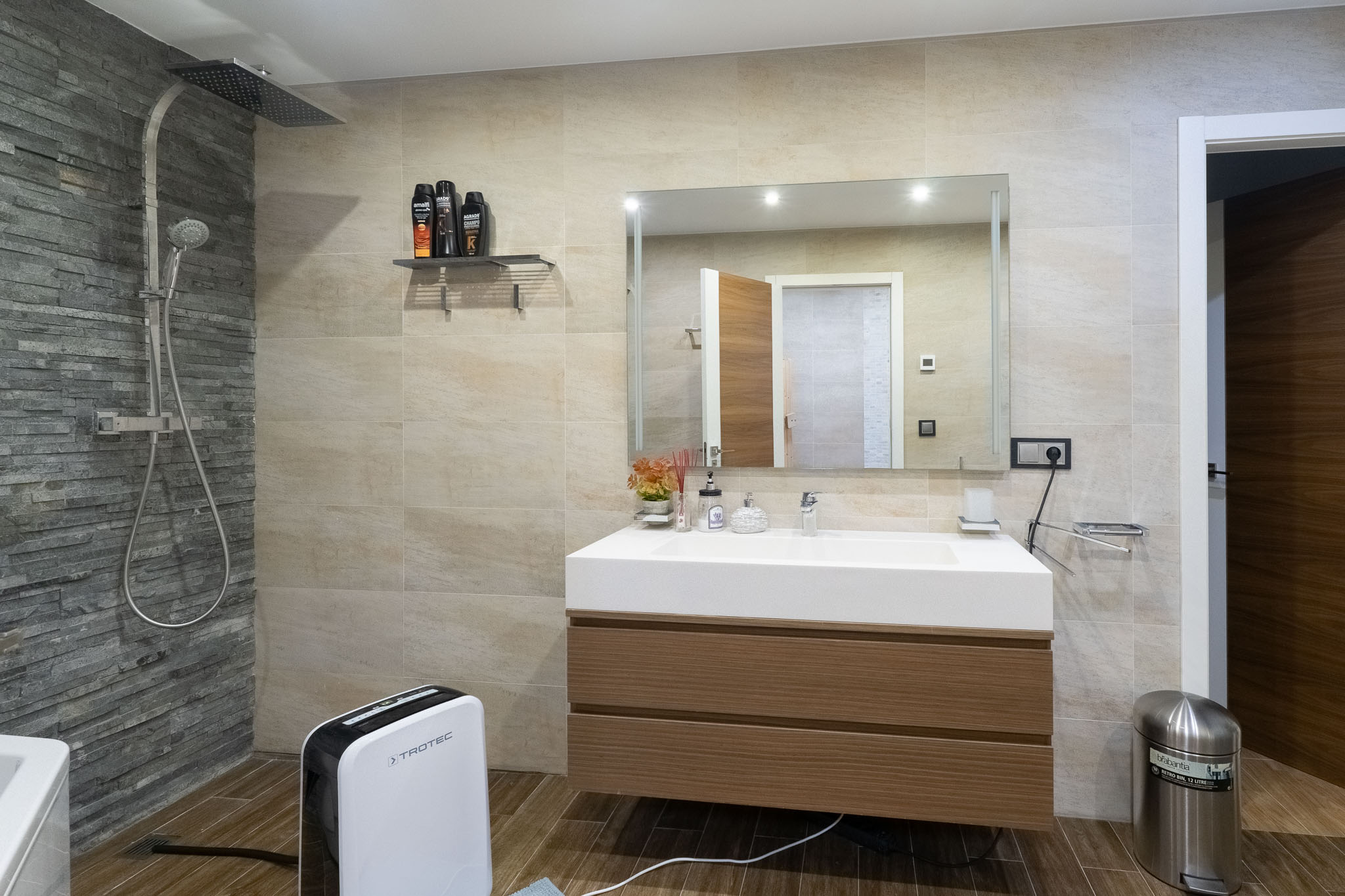 Salle de bain moderne avec douche pluie et mur d'accent en ardoise, meuble vasque suspendu en bois et évier intégré. Carrelage effet bois au sol.