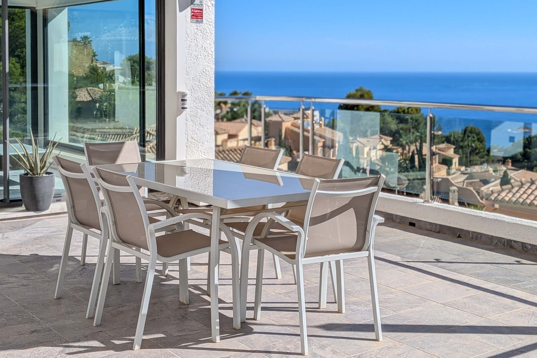 Vaste terrasse extérieure avec table et chaises de salle à manger, offrant des vues panoramiques sur la mer Méditerranée et les toits d'Altea Hills. Des portes coulissantes vitrées mènent à l'intérieur.