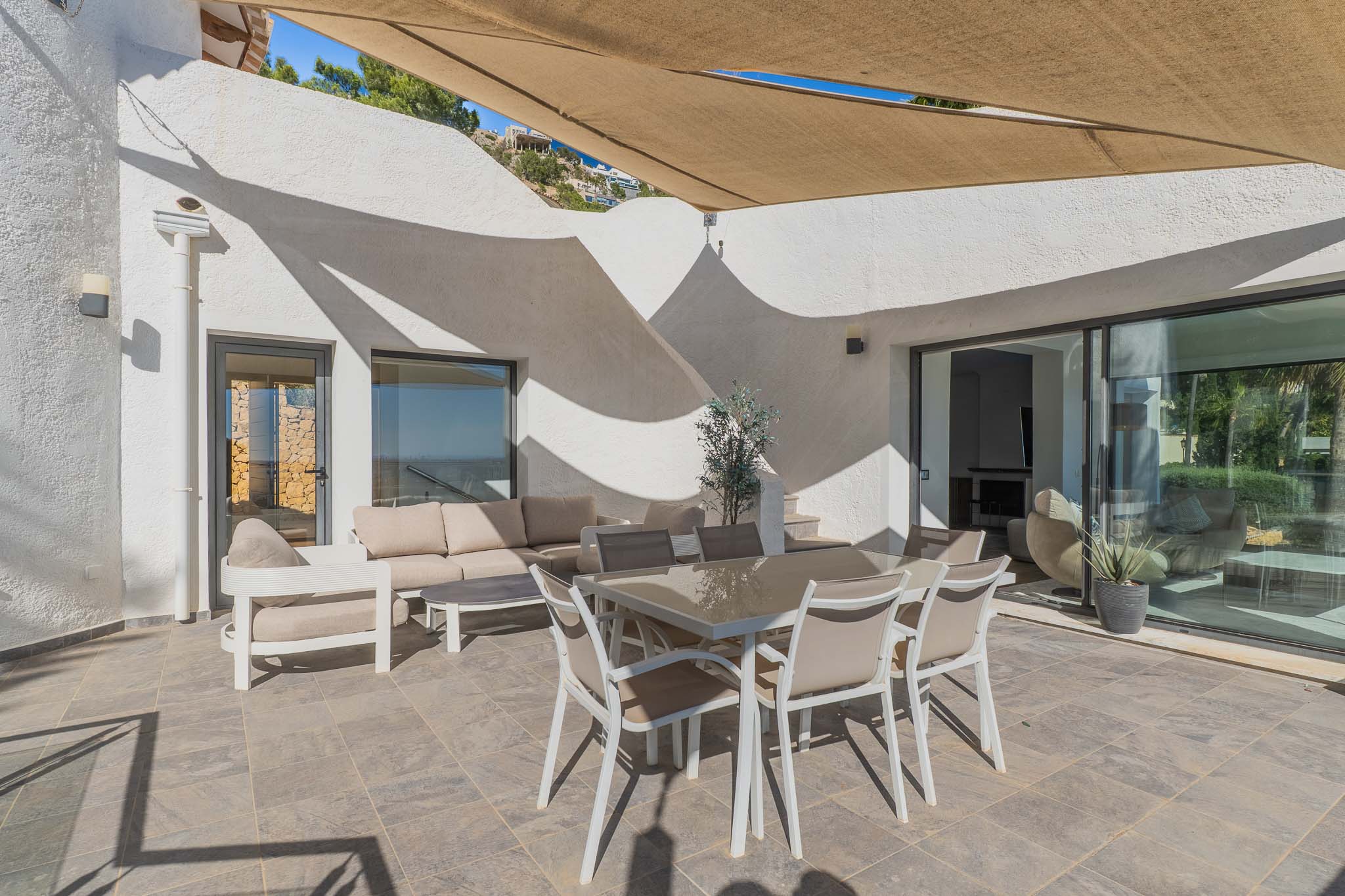 Vaste terrasse extérieure carrelée avec mobilier de salle à manger et salon sous une voile d'ombrage rétractable. Larges baies vitrées vers l'intérieur.