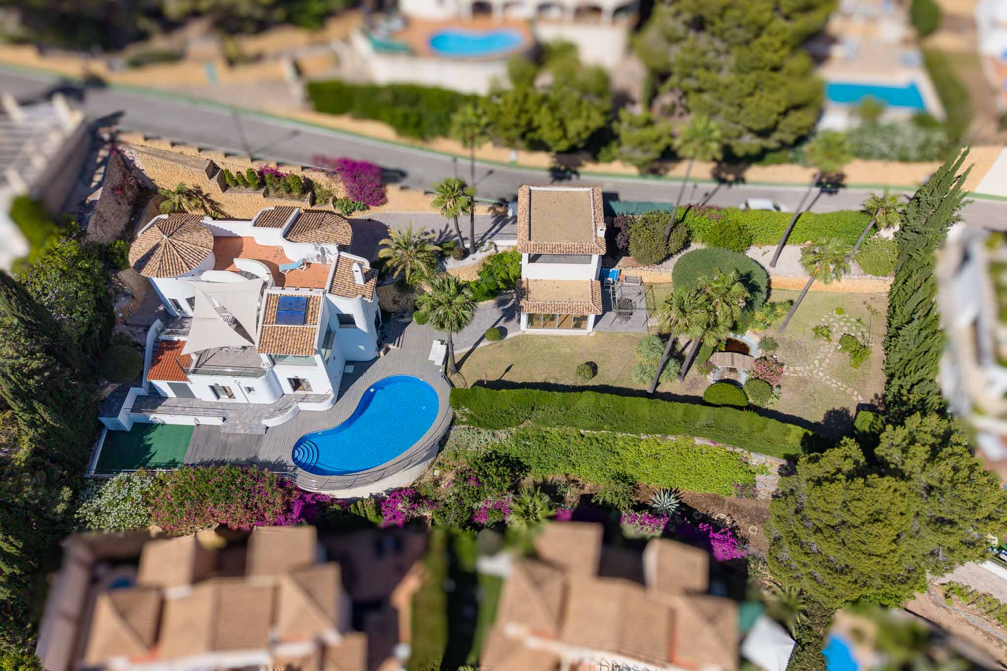 Vue aérienne de la villa, sa piscine de forme irrégulière, de vastes jardins plats avec étang et un bâtiment annexe. Les toits en tuiles et la végétation méditerranéenne luxuriante sont visibles.