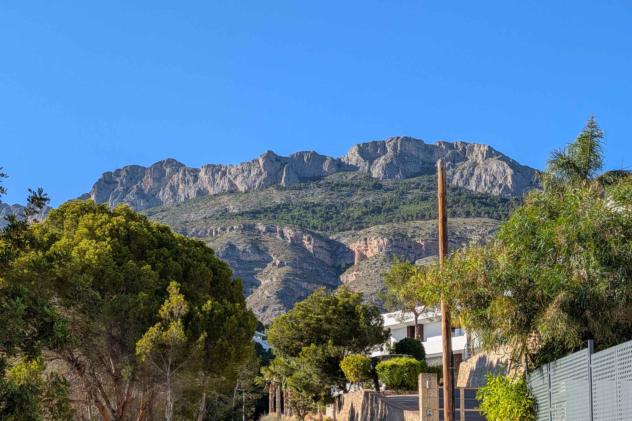 Vue sur la majestueuse Sierra de Bernia, avec ses sommets rocheux et ses pentes verdoyantes, encadrée par la végétation méditerranéenne luxuriante de la propriété.