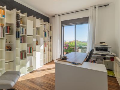 Bureau lumineux avec une bibliothèque modulaire blanche, un sol en bois et un accès à un balcon offrant des vues sur la verdure. Le bureau moderne est baigné de lumière naturelle.