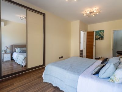Chambre à coucher avec lit aux textiles bleus clairs, parquet stratifié et armoire coulissante à panneau miroir. Un luminaire de plafond moderne et un tableau floral complètent l'espace.