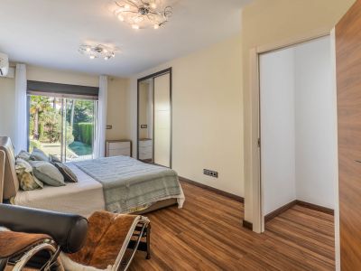 Chambre avec accès direct au jardin par des portes coulissantes vitrées, parquet stratifié et armoire miroir intégrée. Un espace dressing ouvert est visible.