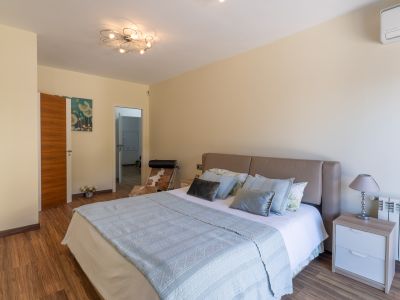 Chambre avec lit à tête de lit beige, parquet stratifié et luminaire de plafond moderne. Une table de chevet avec lampe, un radiateur et la climatisation sont visibles.
