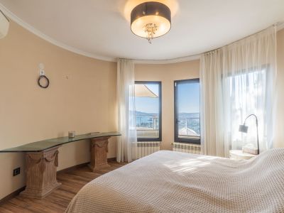 Chambre lumineuse avec vues panoramiques sur la mer, grandes fenêtres à voilages et un bureau en verre sur des socles en bois sculpté.
