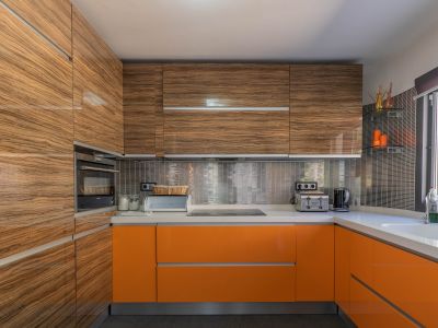 Cuisine moderne avec meubles hauts en bois veiné brillant et bas orange vif, complétée par des plans de travail clairs et une crédence en mosaïque métallique.