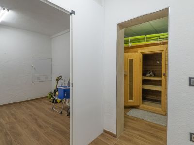 Espace bien-être dédié avec cabine de sauna en bois et bancs intérieurs, adjacent à une buanderie fonctionnelle. Les deux zones partagent un carrelage effet bois.