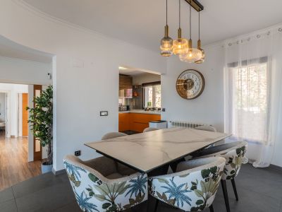 Espace repas avec table effet marbre et chaises à motif tropical. L'éclairage suspendu moderne complète la pièce, ouverte sur une cuisine aux armoires oranges.