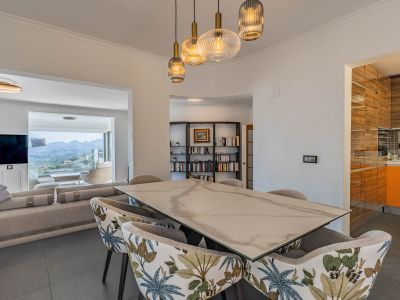 Espace salle à manger design avec table effet marbre et chaises tapissées, éclairé par des suspensions modernes. S'ouvre sur le salon et des vues panoramiques sur la montagne.