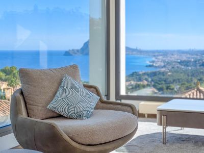 Fauteuil confortable devant une fenêtre panoramique, offrant des vues imprenables sur la mer Méditerranée et le littoral. Le coussin décoratif modernise l'espace intérieur.