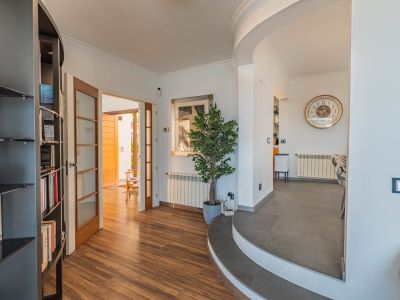 Hall d'entrée avec parquet stratifié effet bois, s'ouvrant sur un espace extérieur par des portes vitrées. Des marches carrelées courbes mènent à la salle à manger, avec une bibliothèque intégrée.