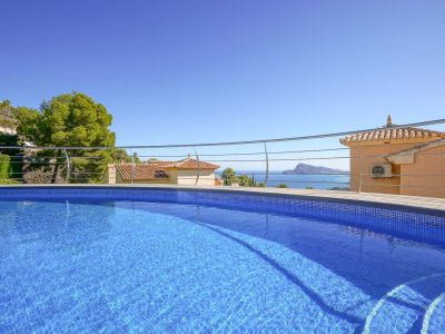 Piscine en mosaïque bleue avec escaliers intégrés et balustrade moderne, encadrant des vues panoramiques sur la mer, des toits traditionnels et la côte.