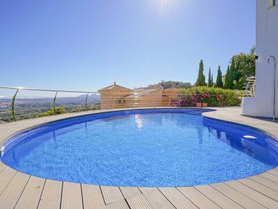 Piscine incurvée en mosaïque bleue, entourée d'une terrasse en bois clair, avec une balustrade en acier inoxydable et vue panoramique sur la vallée et la ville.