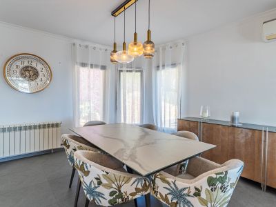 Salle à manger lumineuse avec table effet marbre, chaises à motif tropical et lustre linéaire moderne, baignée de lumière naturelle.