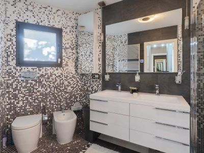 Salle de bain contemporaine avec murs et sol en mosaïque tons terre/gris. Double vasque blanche, grand miroir éclairé, WC et bidet suspendus, plus un sèche-serviettes mural.