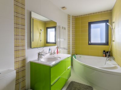 Salle de bain moderne avec baignoire d'angle et meuble-lavabo vert vif. Carrelage mural blanc texturé, vert lime et mosaïque à carreaux. Fenêtre et sèche-serviettes mural.