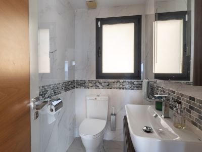 Salle de bain moderne avec carrelage effet marbre blanc, une frise mosaïque grise et une fenêtre à cadre sombre. Comprend un lavabo blanc et des toilettes assorties.