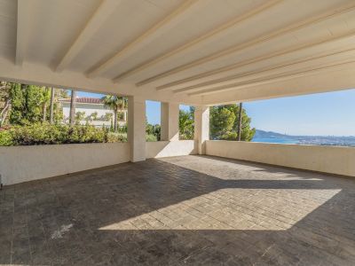 Vaste abri pour voitures couvert avec sol en béton estampé et plafond à poutres blanches. Il offre une vue panoramique sur la mer Méditerranée et la côte, encadrée de verdure luxuriante.