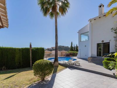 Vaste jardin avec piscine circulaire et solarium en bois, bordé par une villa blanche et une haie dense. Vues sur les collines environnantes.