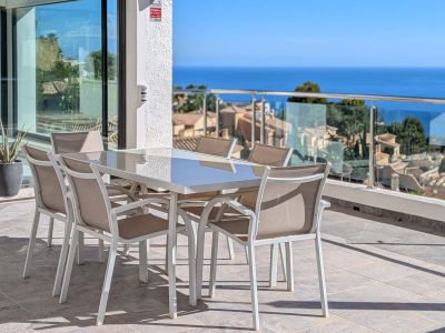 Vaste terrasse extérieure avec table et chaises de salle à manger, offrant des vues panoramiques sur la mer Méditerranée et les toits d'Altea Hills. Des portes coulissantes vitrées mènent à l'intérieur.