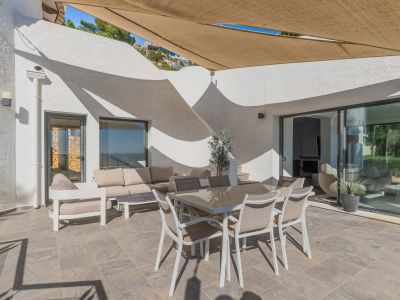 Vaste terrasse extérieure carrelée avec mobilier de salle à manger et salon sous une voile d'ombrage rétractable. Larges baies vitrées vers l'intérieur.