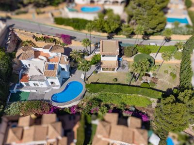 Vue aérienne de la villa, sa piscine de forme irrégulière, de vastes jardins plats avec étang et un bâtiment annexe. Les toits en tuiles et la végétation méditerranéenne luxuriante sont visibles.