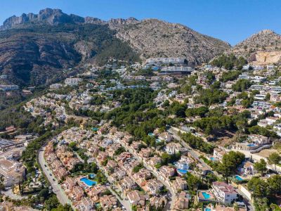 Vue aérienne panoramique d'Altea Hills, présentant de nombreuses villas avec piscines sur la colline verdoyante, adossées à des montagnes imposantes.