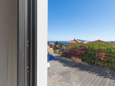 Vue depuis la porte coulissante sur la terrasse en composite, aperçu de la piscine et garde-corps en acier. La mer Méditerranée et les toits traditionnels sont visibles en arrière-plan.