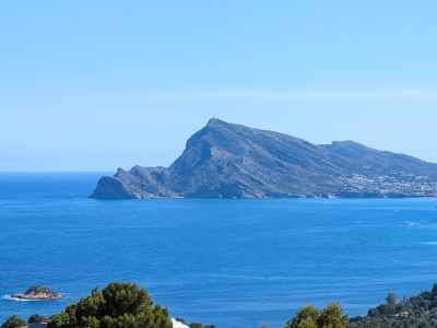 Vue panoramique sur la Méditerranée, avec le profil imposant de la Sierra Helada, une ville côtière lointaine et de petits îlots rocheux sous un ciel azur.