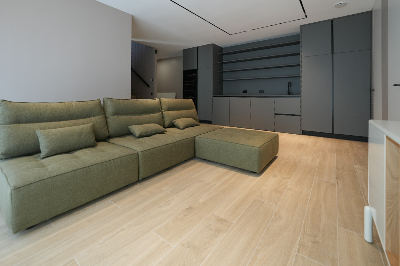 Canapé modulaire vert olive dans un espace de vie ouvert avec carrelage imitation bois clair. Meubles intégrés gris foncé avec évier et étagères en arrière-plan. Canapé modulaire vert olive dans un espace de vie ouvert avec carrelage imitation bois clair. Meubles intégrés gris foncé avec évier et étagères en arrière-plan.