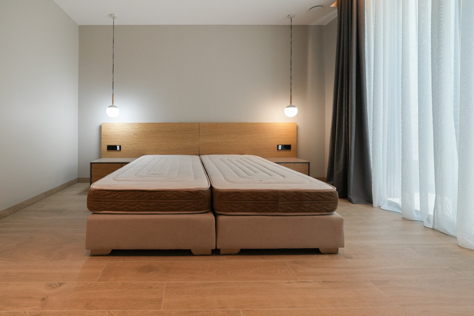 Chambre avec lit double composé de deux sommiers tapissiers, tête de lit en bois clair intégrant des tables de chevet et deux suspensions modernes. Grande fenêtre voilée. Chambre avec lit double composé de deux sommiers tapissiers, tête de lit en bois clair intégrant des tables de chevet et deux suspensions modernes. Grande fenêtre voilée.