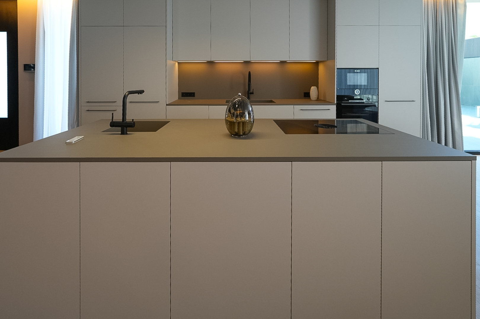 Cuisine design avec îlot central, évier intégré, plaque à induction et mobilier aux tons neutres. Cuisine design avec îlot central, évier intégré, plaque à induction et mobilier aux tons neutres.
