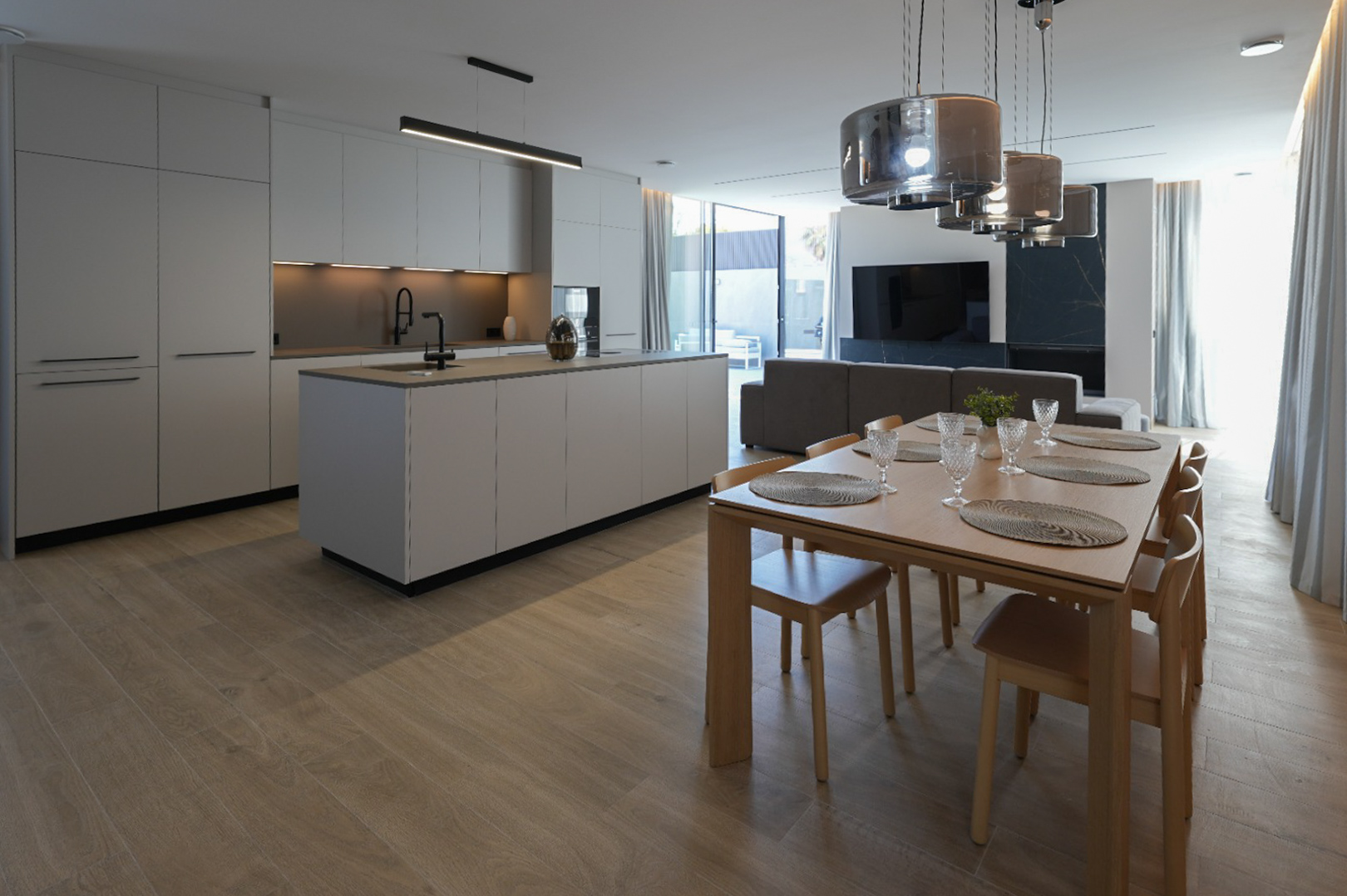 Cuisine design minimaliste avec îlot central et robinetterie noire, ouverte sur une élégante salle à manger en bois avec six chaises et suspensions modernes. Cuisine design minimaliste avec îlot central et robinetterie noire, ouverte sur une élégante salle à manger en bois avec six chaises et suspensions modernes.