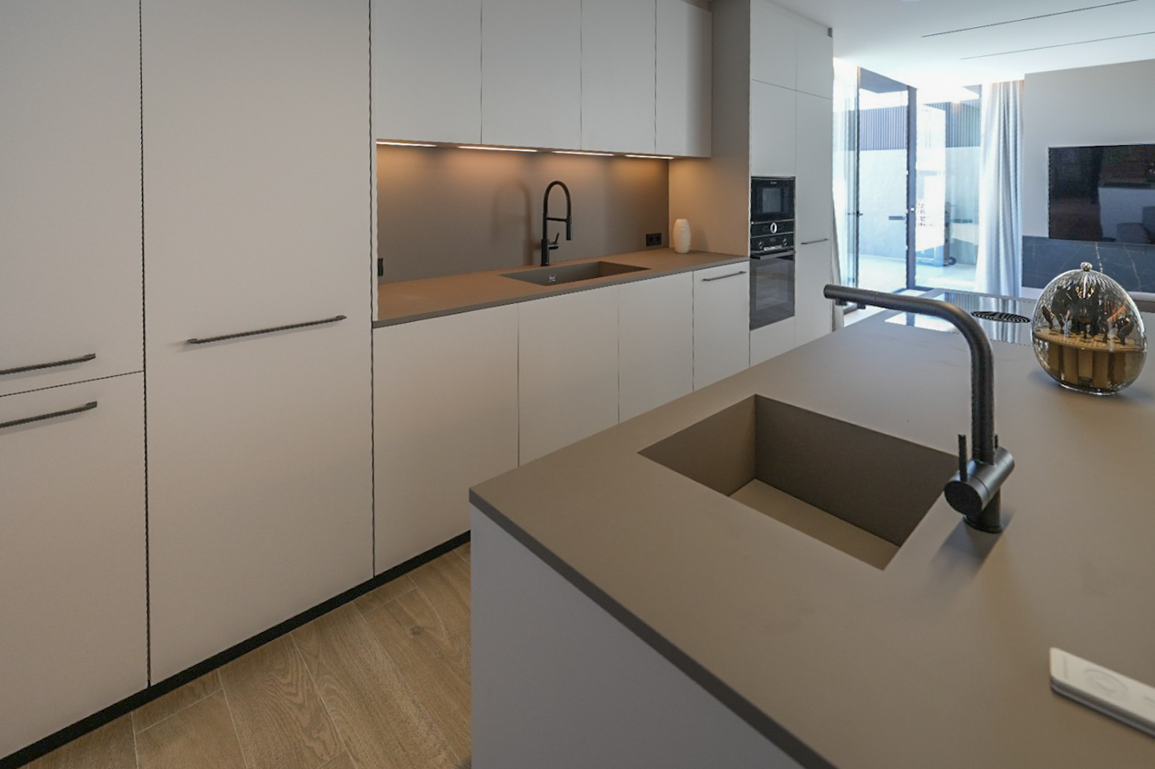Cuisine moderne avec îlot central et double évier intégré. Armoires minimalistes aux tons neutres, appareils encastrés et parquet clair, s'ouvrant sur l'extérieur. Cuisine moderne avec îlot central et double évier intégré. Armoires minimalistes aux tons neutres, appareils encastrés et parquet clair, s'ouvrant sur l'extérieur.