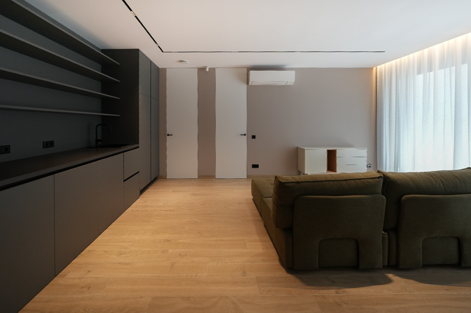 Espace de vie moderne avec kitchenette intégrée gris foncé, sol imitation bois clair et canapé modulaire vert. Portes affleurantes et lumière naturelle. Espace de vie moderne avec kitchenette intégrée gris foncé, sol imitation bois clair et canapé modulaire vert. Portes affleurantes et lumière naturelle.