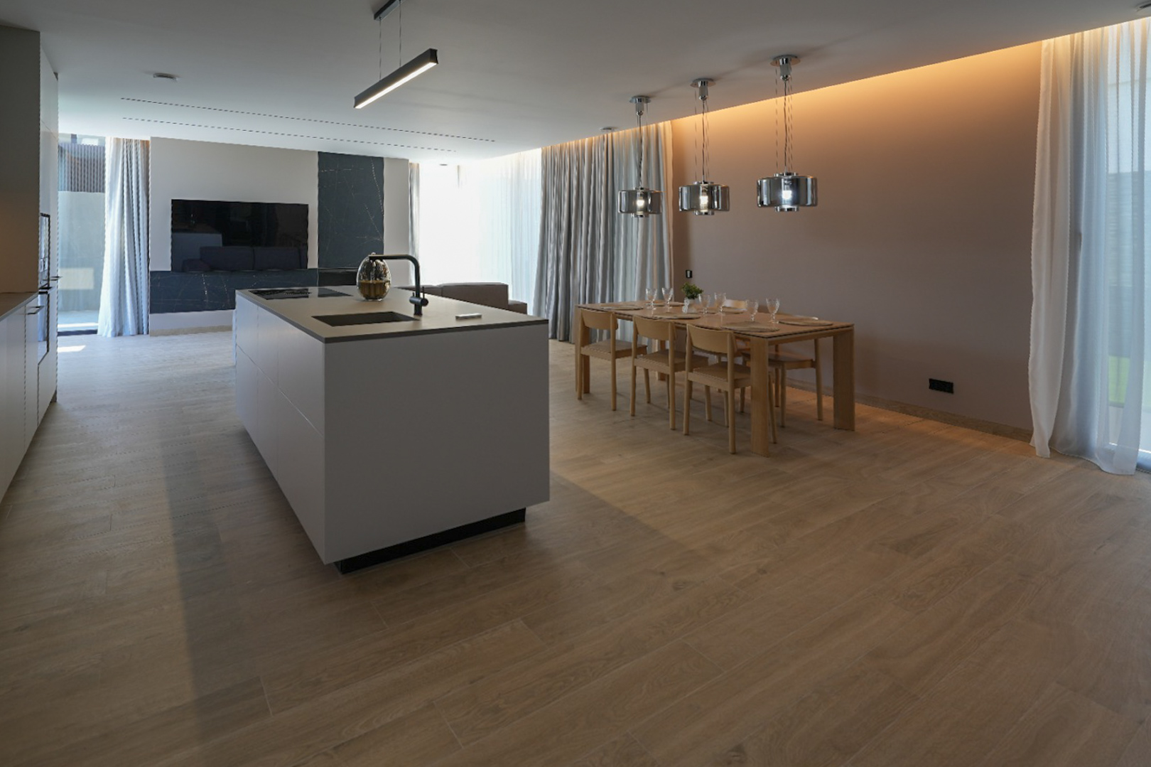 Îlot de cuisine moderne avec évier intégré et plaque de cuisson, ouvert sur une salle à manger avec table en bois et luminaires suspendus. Sol carrelé imitation bois clair. Îlot de cuisine moderne avec évier intégré et plaque de cuisson, ouvert sur une salle à manger avec table en bois et luminaires suspendus. Sol carrelé imitation bois clair.