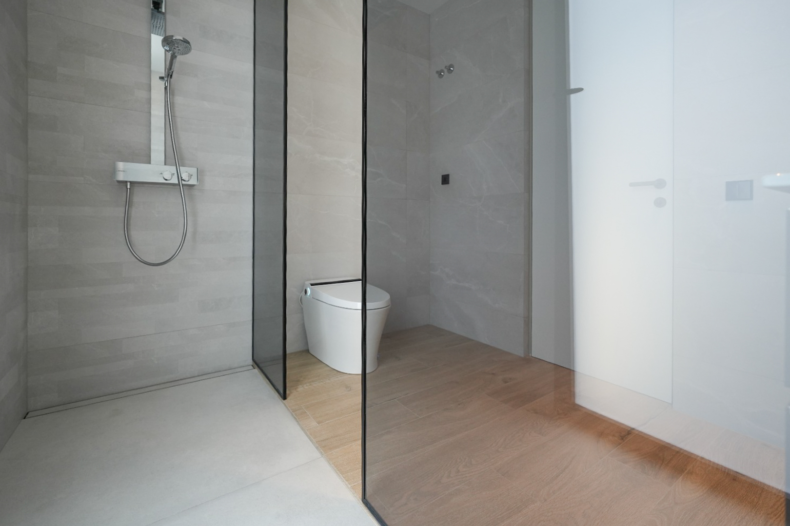 Salle de bain moderne avec douche à l'italienne, carrelage gris clair et mitigeur thermostatique chromé. Une paroi vitrée sépare la douche des toilettes intelligentes avec carrelage imitation bois. Salle de bain moderne avec douche à l'italienne, carrelage gris clair et mitigeur thermostatique chromé. Une paroi vitrée sépare la douche des toilettes intelligentes avec carrelage imitation bois.