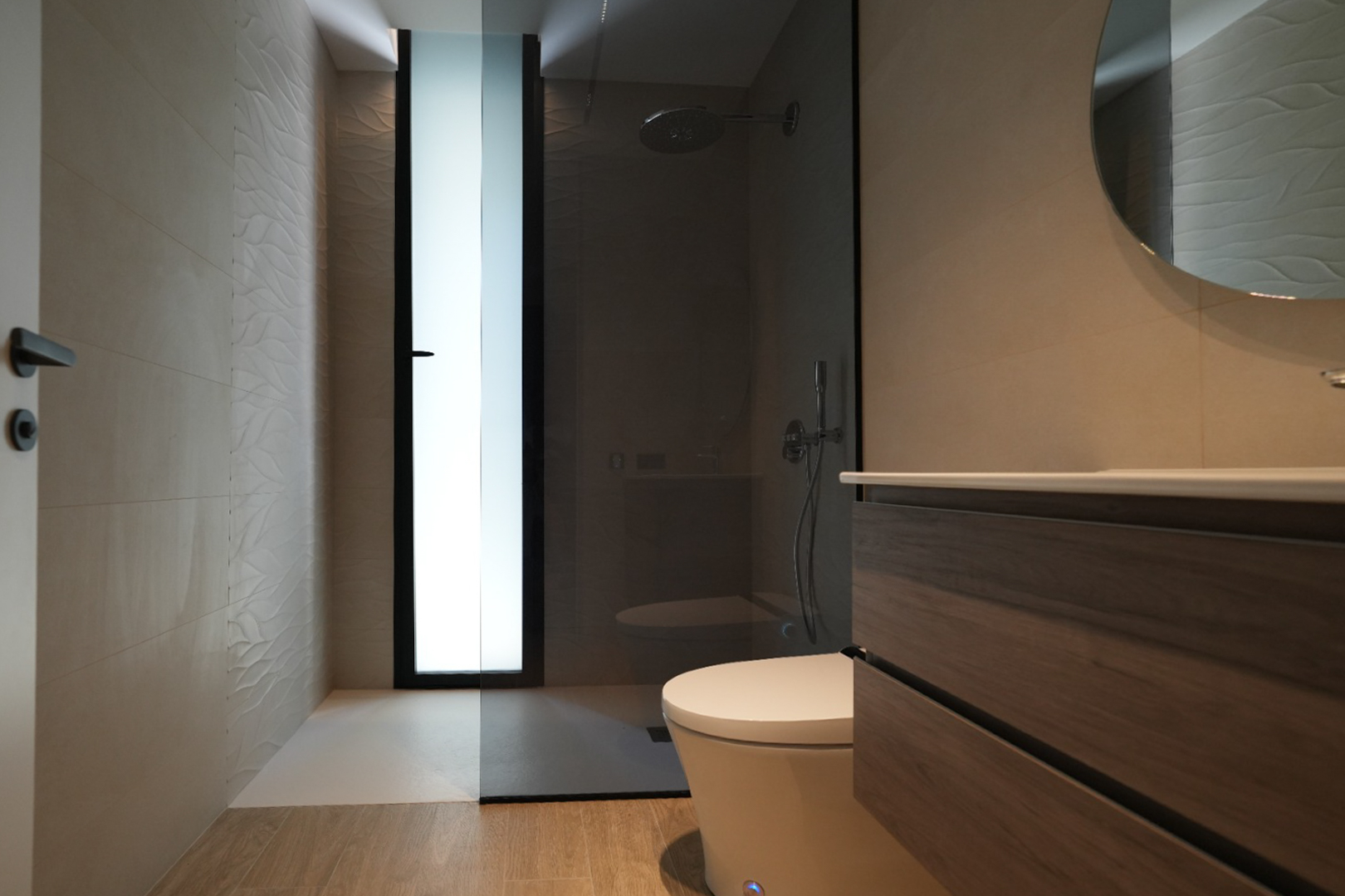 Salle de bain moderne avec meuble-lavabo en bois, miroir rond et douche à l'italienne. Carrelage mural texturé et fenêtre dépolie. Salle de bain moderne avec meuble-lavabo en bois, miroir rond et douche à l'italienne. Carrelage mural texturé et fenêtre dépolie.