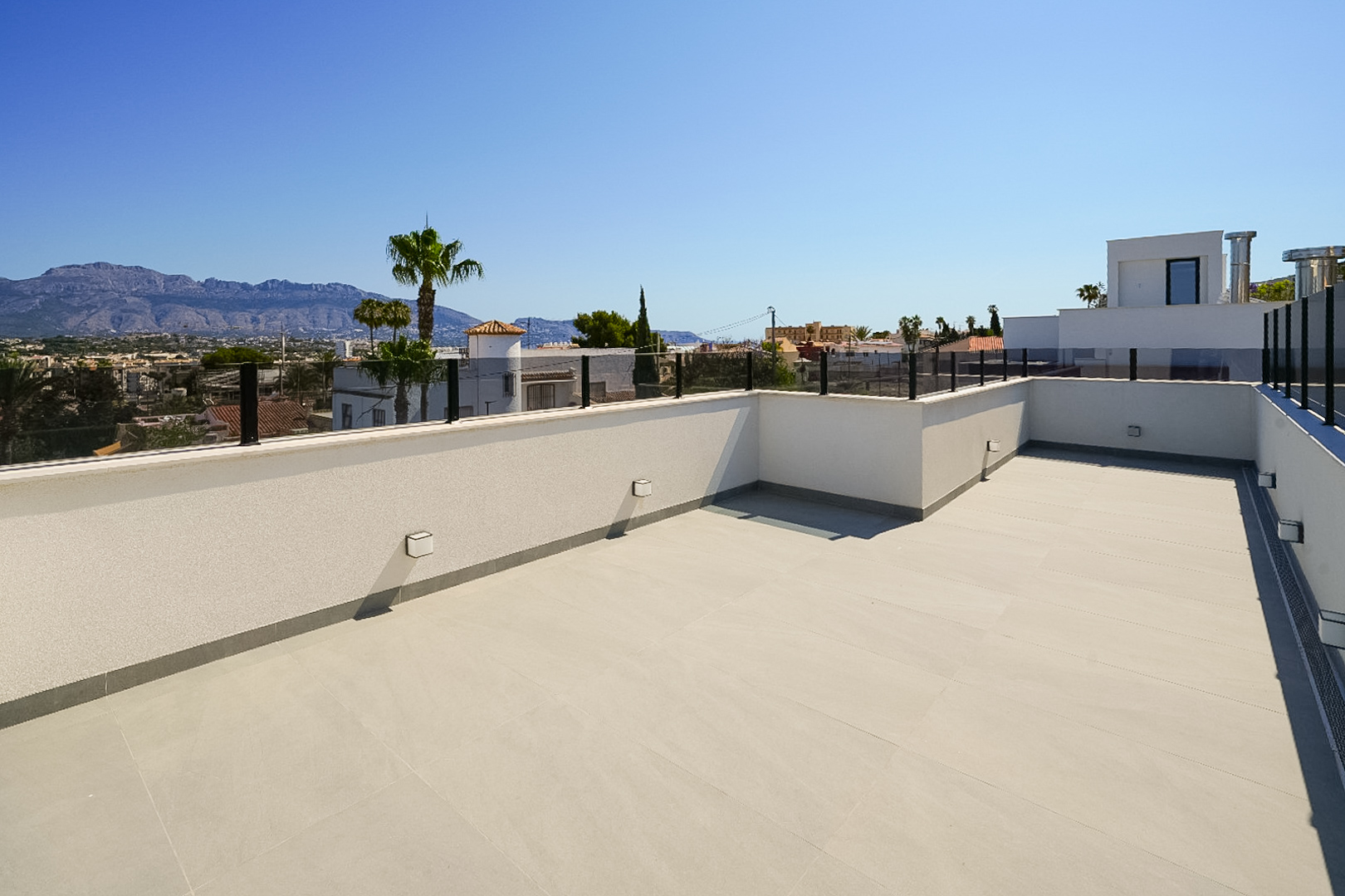 Vaste terrasse sur le toit avec carrelage clair et garde-corps en verre moderne, offrant des vues panoramiques sur les montagnes et la ville.