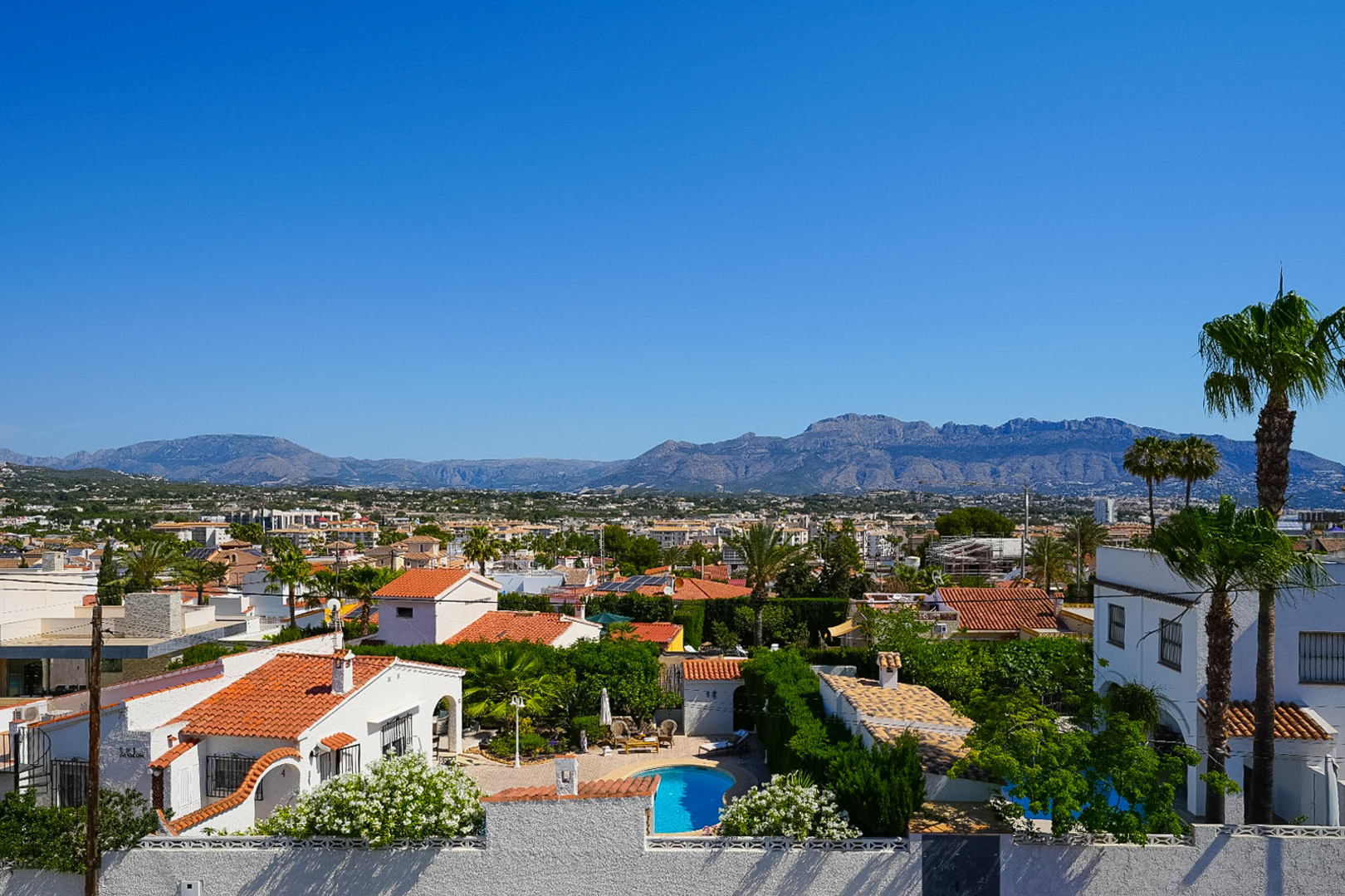 Vue aérienne du quartier résidentiel d'Albir, montrant une piscine privée, des maisons aux toits de tuiles et une végétation méditerranéenne luxuriante, avec les montagnes en toile de fond. Vue aérienne du quartier résidentiel d'Albir, montrant une piscine privée, des maisons aux toits de tuiles et une végétation méditerranéenne luxuriante, avec les montagnes en toile de fond.